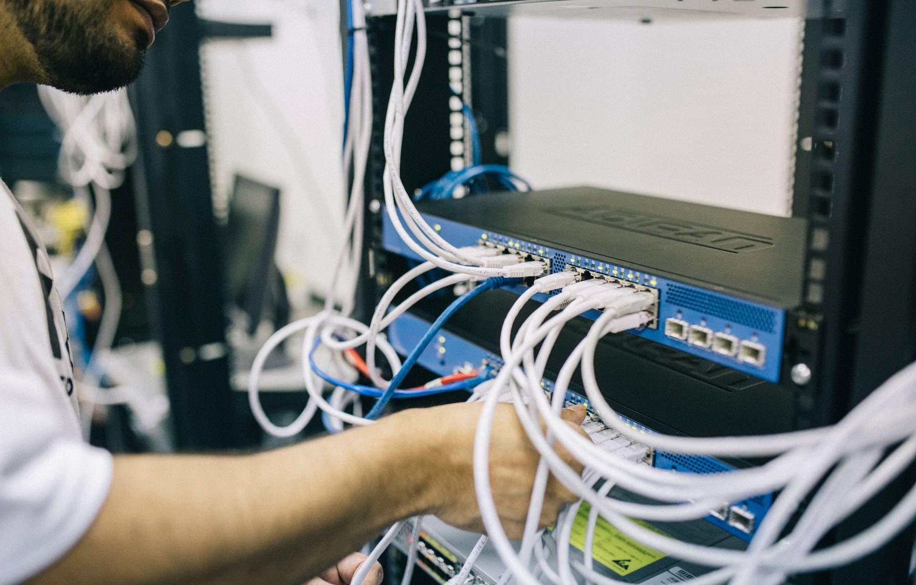An engineer patching cables into a rack-mounted switch inside a network cabinet