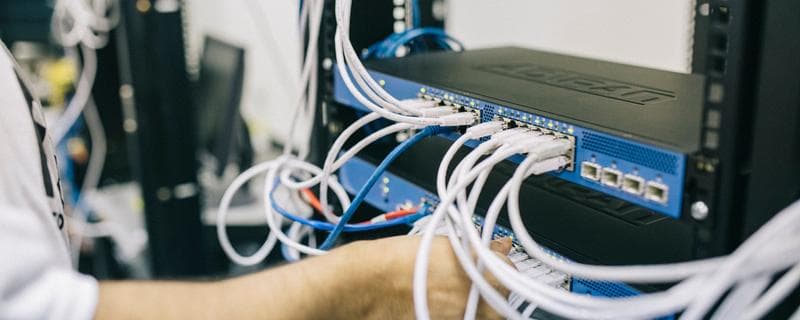 An engineer patching cables into a rack-mounted switch inside a network cabinet